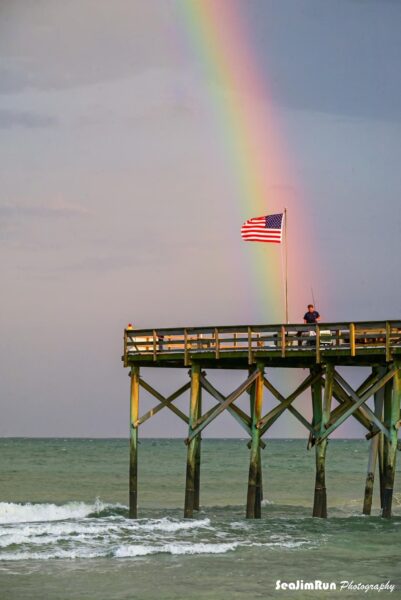 A Majestic Display: Rainbow and American Flag Over South Carolina Pier